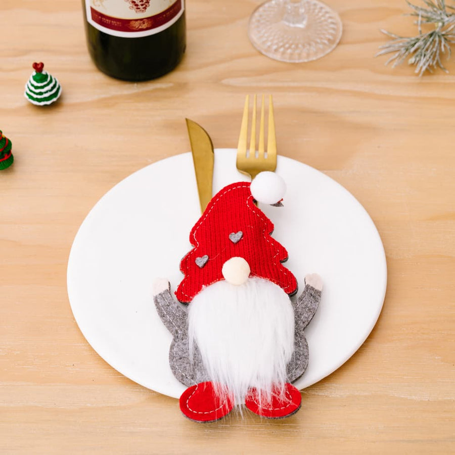 Red festive gnome cutlery accoutrement with white beard and grey arms on a plate.