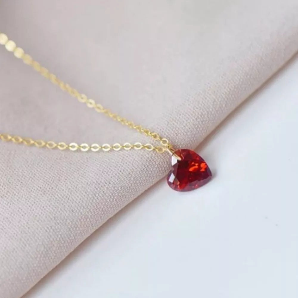 Gold chain necklace with a faceted red heart-shaped zircon pendant.