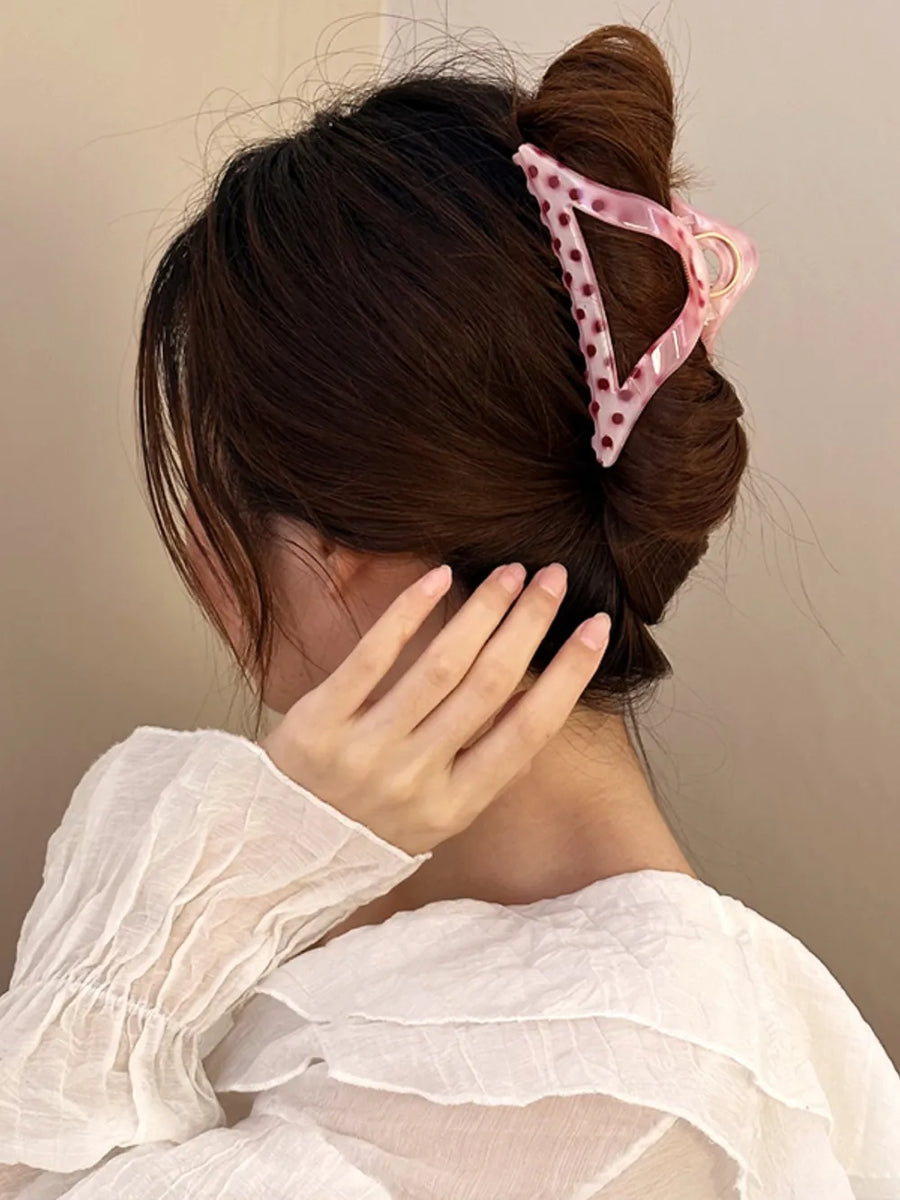 Polka dot claw hair clip in pink with dark red dots, triangular shape.