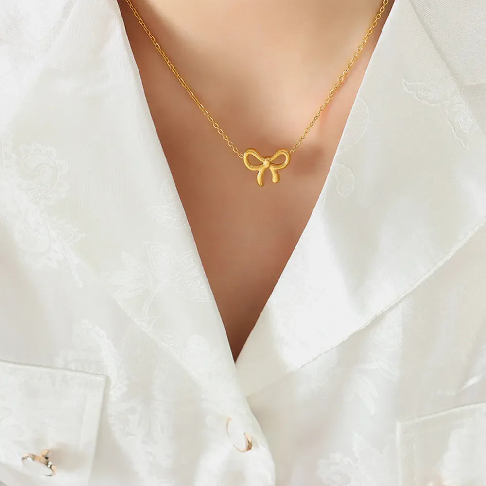 Delicate gold bow pendant necklace on a fine chain, styled with a white textured shirt.