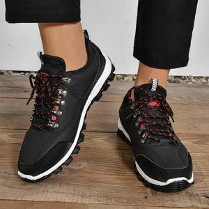 Black lace-up low-top sneakers with patterned red and black laces and white soles.