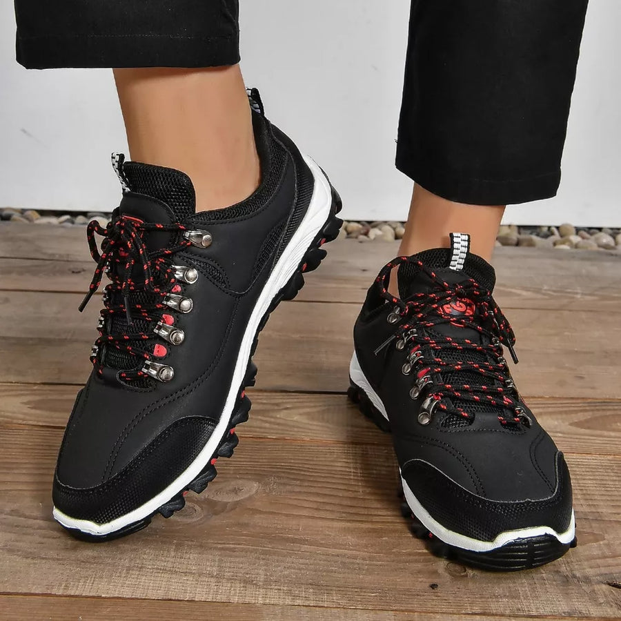 Black lace-up low-top sneakers with patterned red and black laces and white soles.