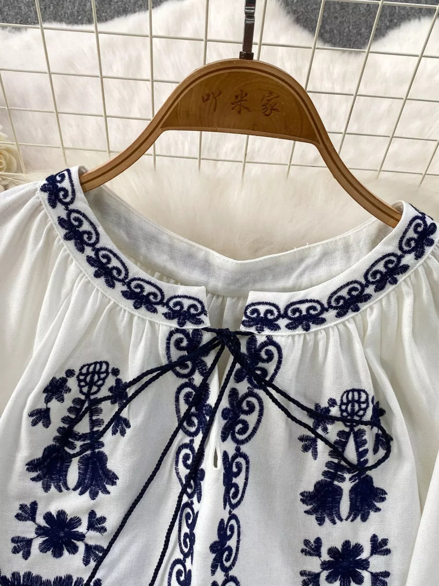 White tie-neck blouse with intricate navy embroidery and balloon sleeves.