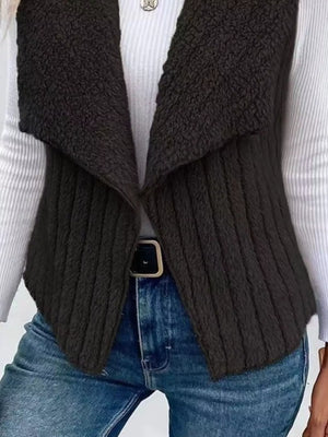 Black fleece vest with open front and ribbed knit body, styled with jeans.