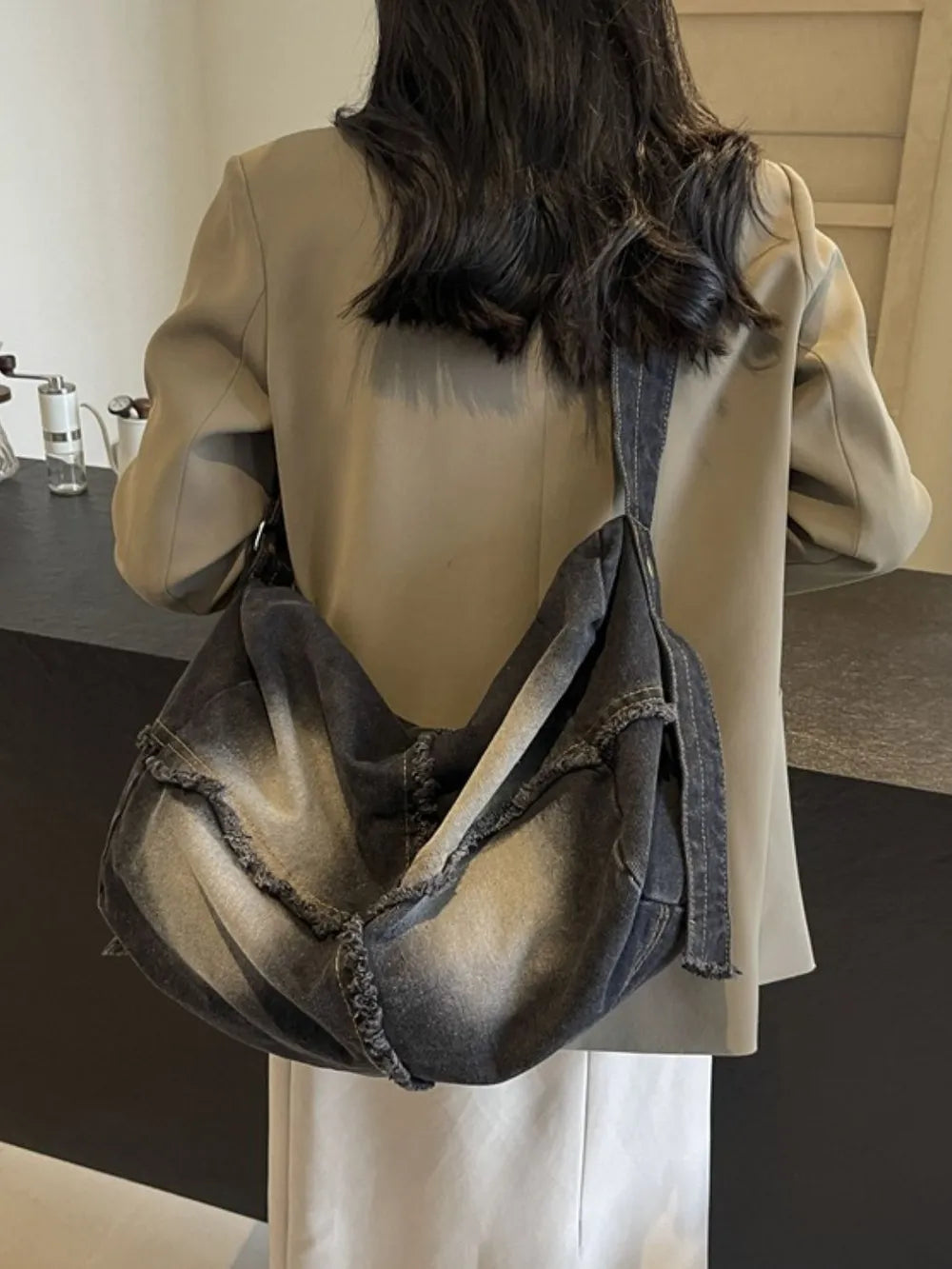 Frayed denim slouch crossbody bag in dark wash with distressed edges.