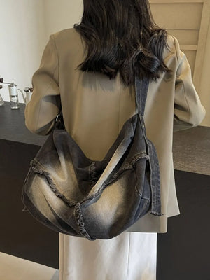 Frayed denim slouch crossbody bag in dark wash with distressed edges.