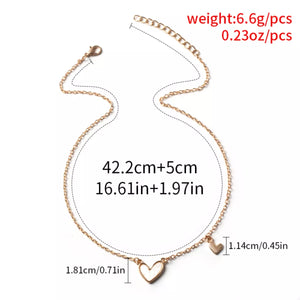 Gold alloy necklace with two heart pendants, one larger with white inlay.