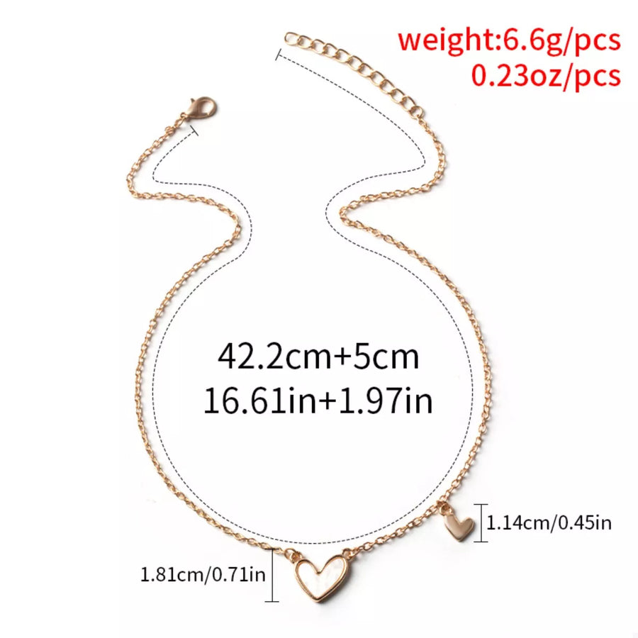 Gold alloy necklace with two heart pendants, one larger with white inlay.
