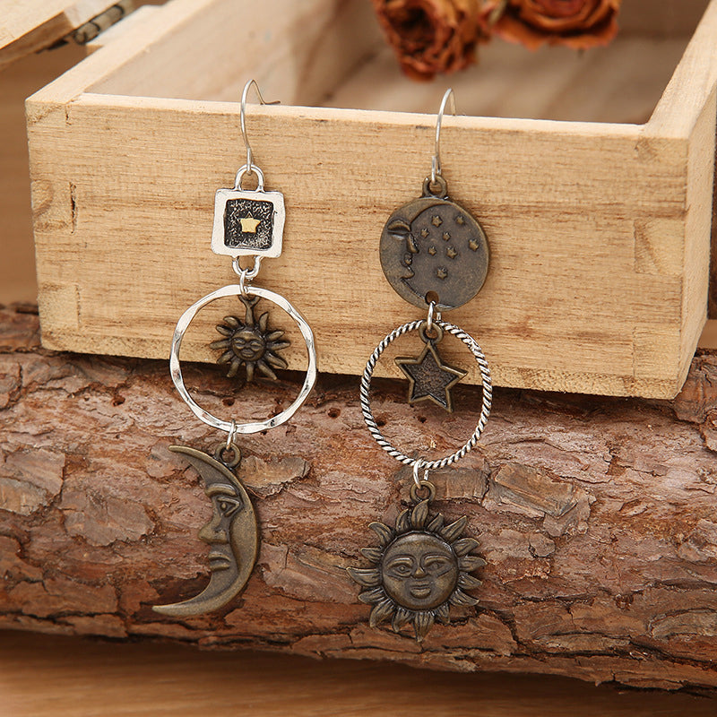 Asymmetrical drop earrings with sun, moon, and star charms in copper tones.
