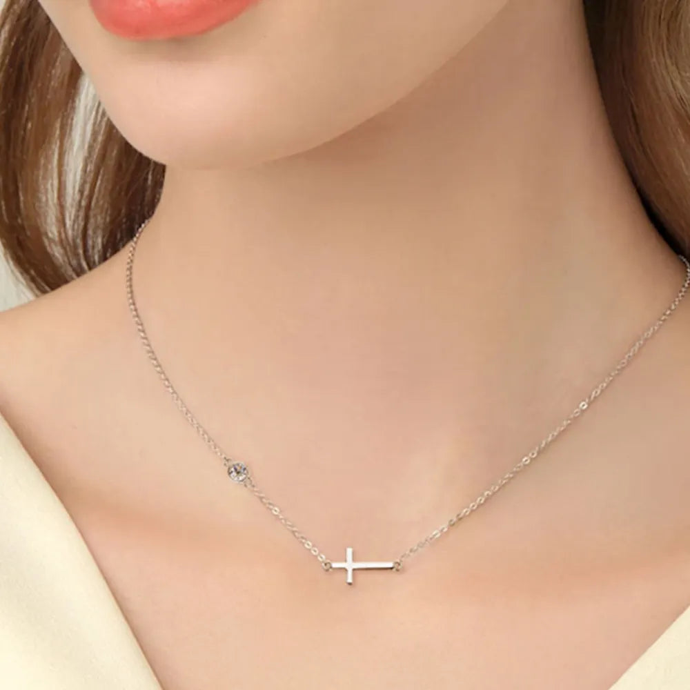 Silver asymmetrical cross pendant necklace with a single stone accent.