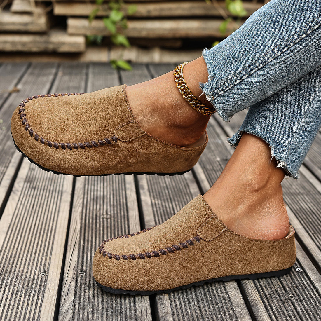 Brown slip-on flats with round toe and decorative stitching, styled with jeans and an anklet.