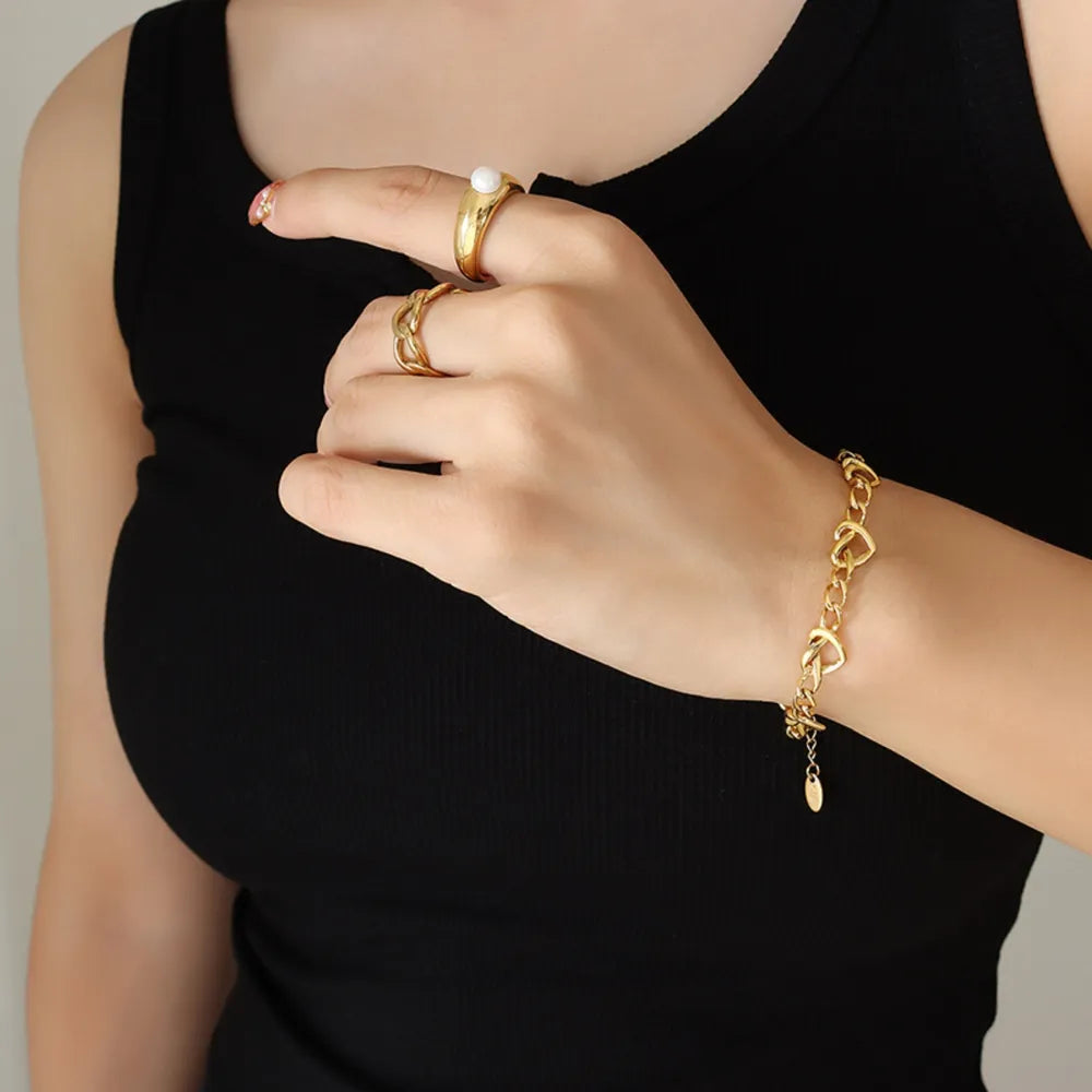 Gold heart link chain bracelet with a small charm, styled with rings.