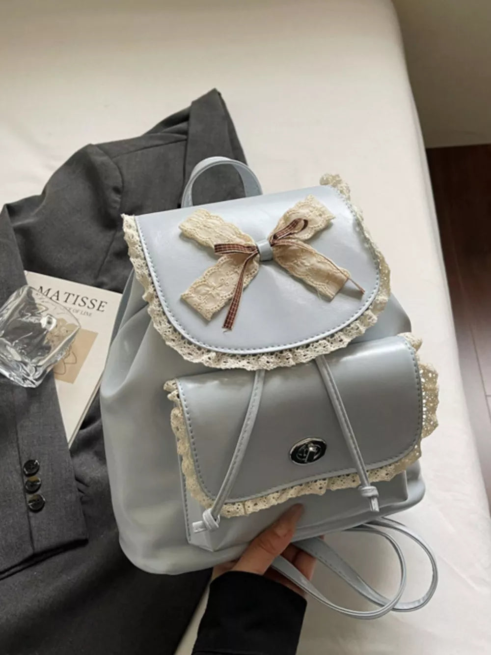 Blue mini backpack with lace trim, bow, and buckle closure.