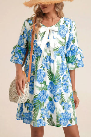Ruffled mini dress with hydrangea and palm print, white bow neckline, and tiered sleeves.