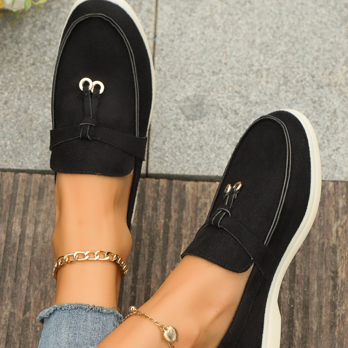 Black flat slip-ons with decorative strap and gold hardware detail.