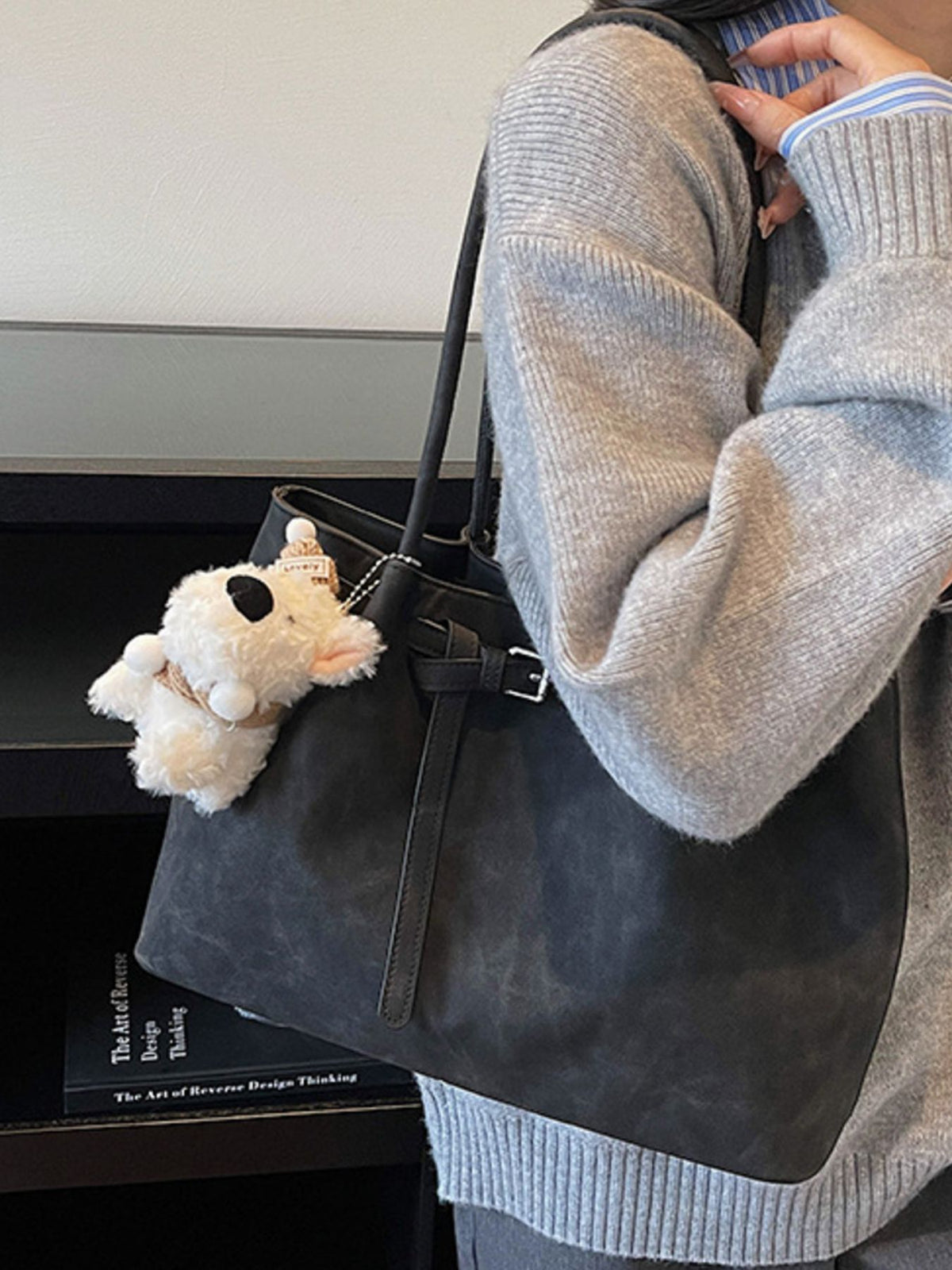 Black shoulder bag with buckle accent and a fluffy keychain charm.