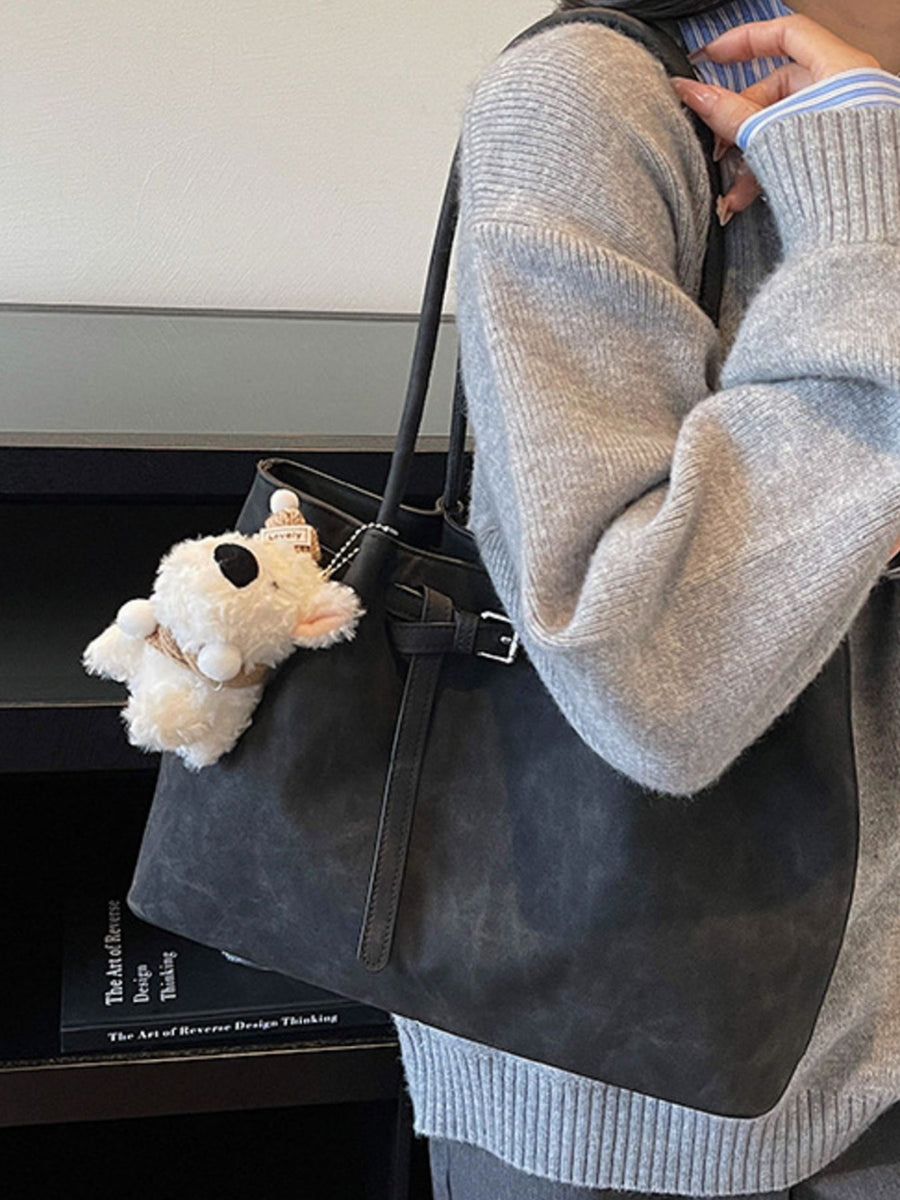 Black shoulder bag with buckle accent and a fluffy keychain charm.