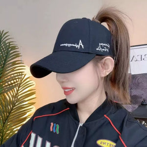 Black baseball cap with white embroidered letter A and script details, worn by a woman with a ponytail.