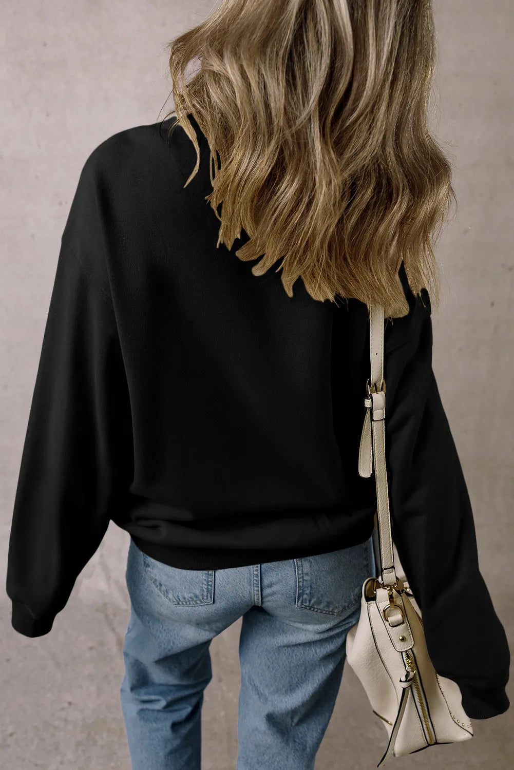Black crewneck sweatshirt with long sleeves, casual fit, worn with jeans and a cream crossbody bag.
