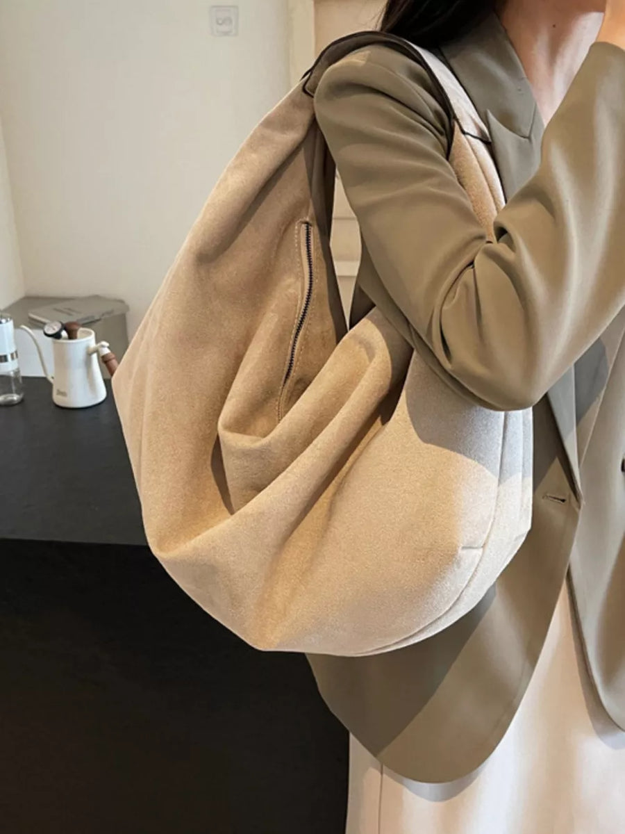 Spacious off-white suede shoulder bag with exterior zipper pocket.