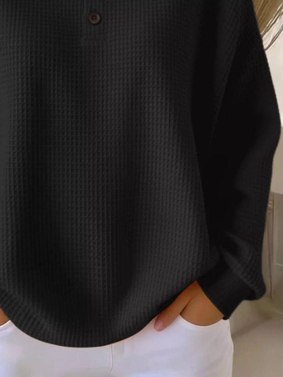 Black waffle knit top with button detail and long sleeves, paired with white pants.
