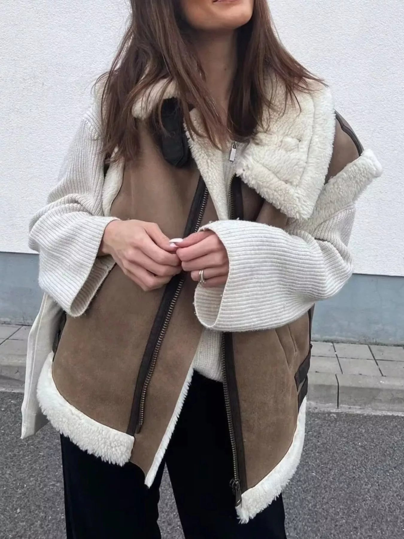 Brown faux shearling vest coat with white trim and zipper details, styled with a cream sweater.