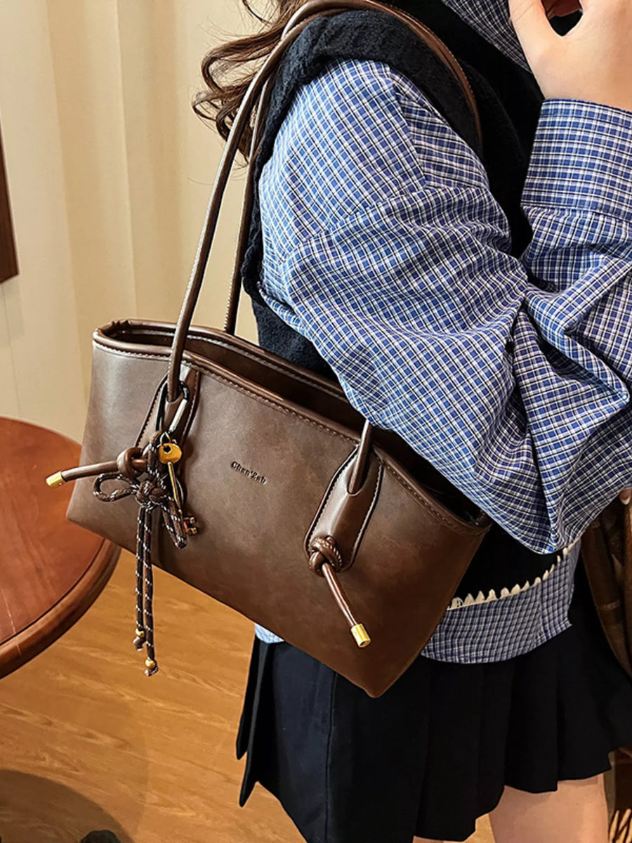 Brown leather shoulder bag with decorative knot and charm detail