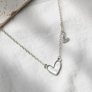 Silver necklace with a white heart pendant and a small dangling heart charm.