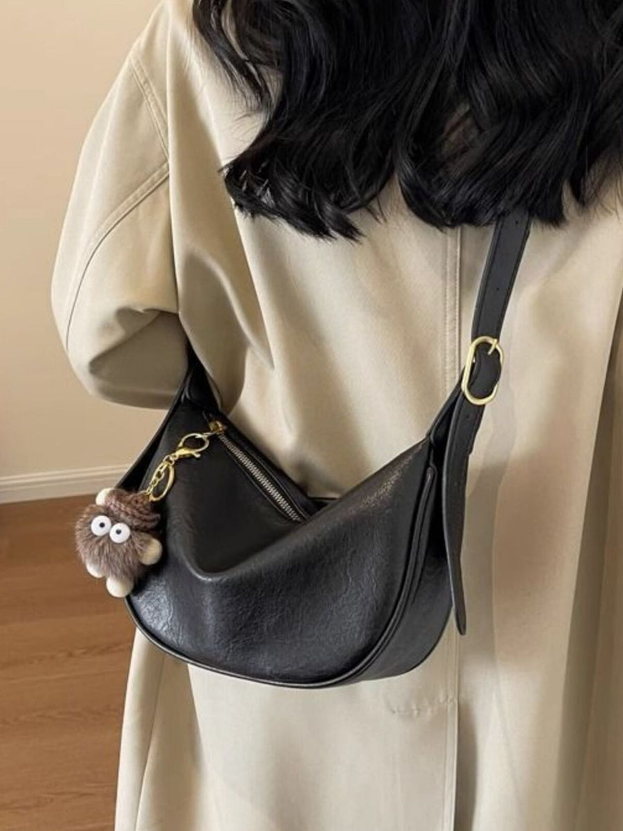 Black crescent shoulder bag with plush charm and adjustable strap