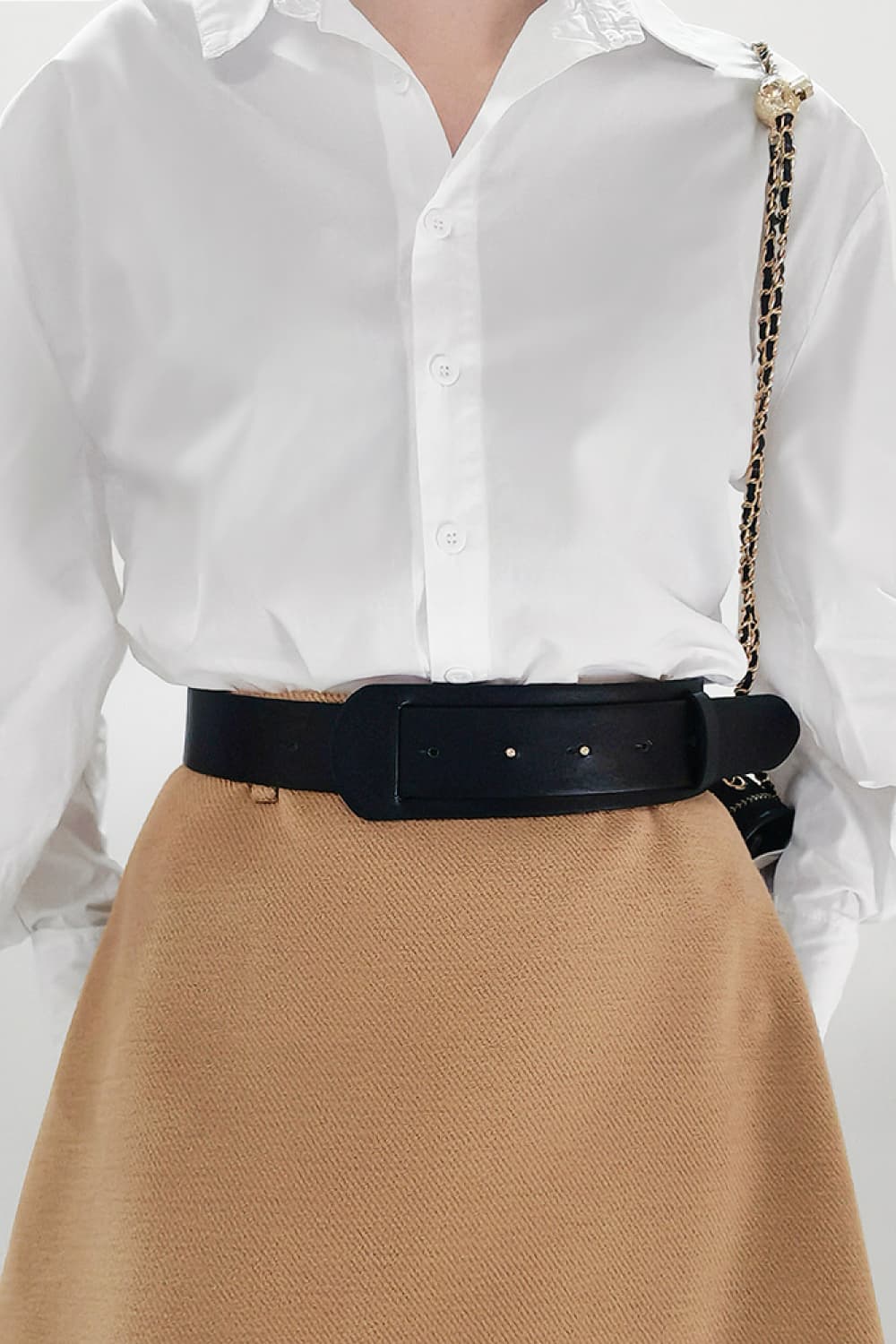 Sculpted black leather waist belt with a wide buckle, worn over a white shirt and tan skirt.