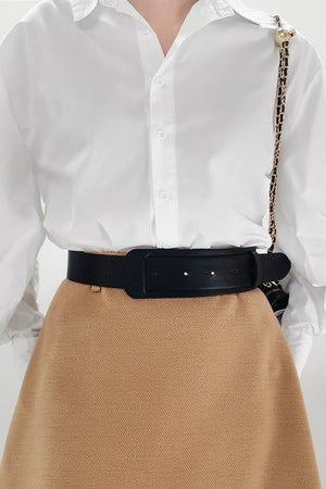 Sculpted black leather waist belt with a wide buckle, worn over a white shirt and tan skirt.