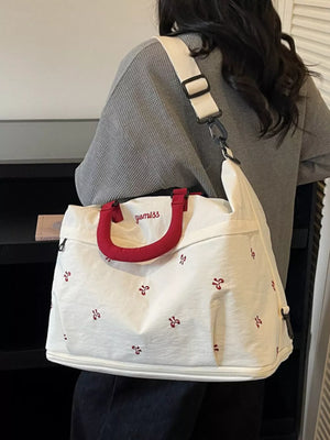 White tote bag with red floral embroidery and red handles, worn with a grey sweater.