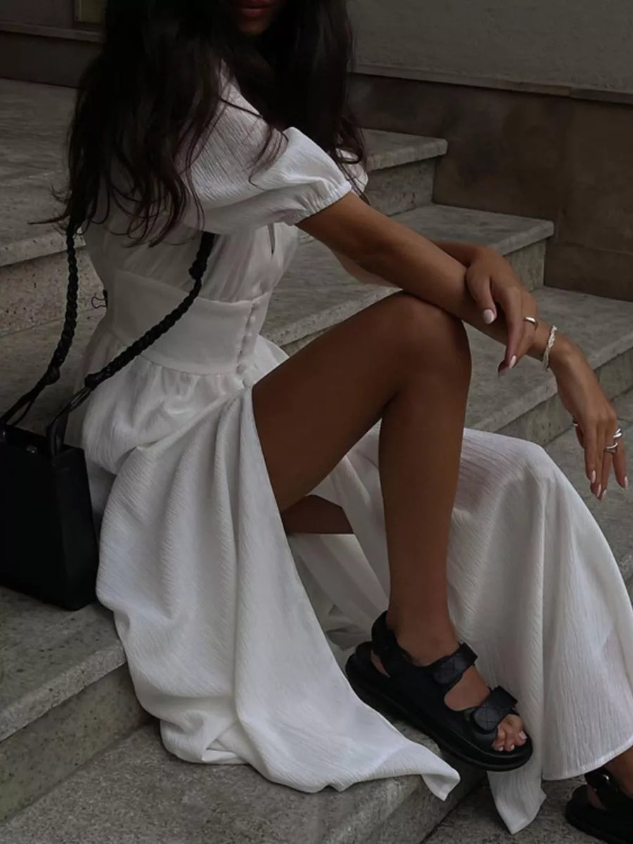 White textured maxi dress with puff sleeves and a high slit, styled with black sandals.