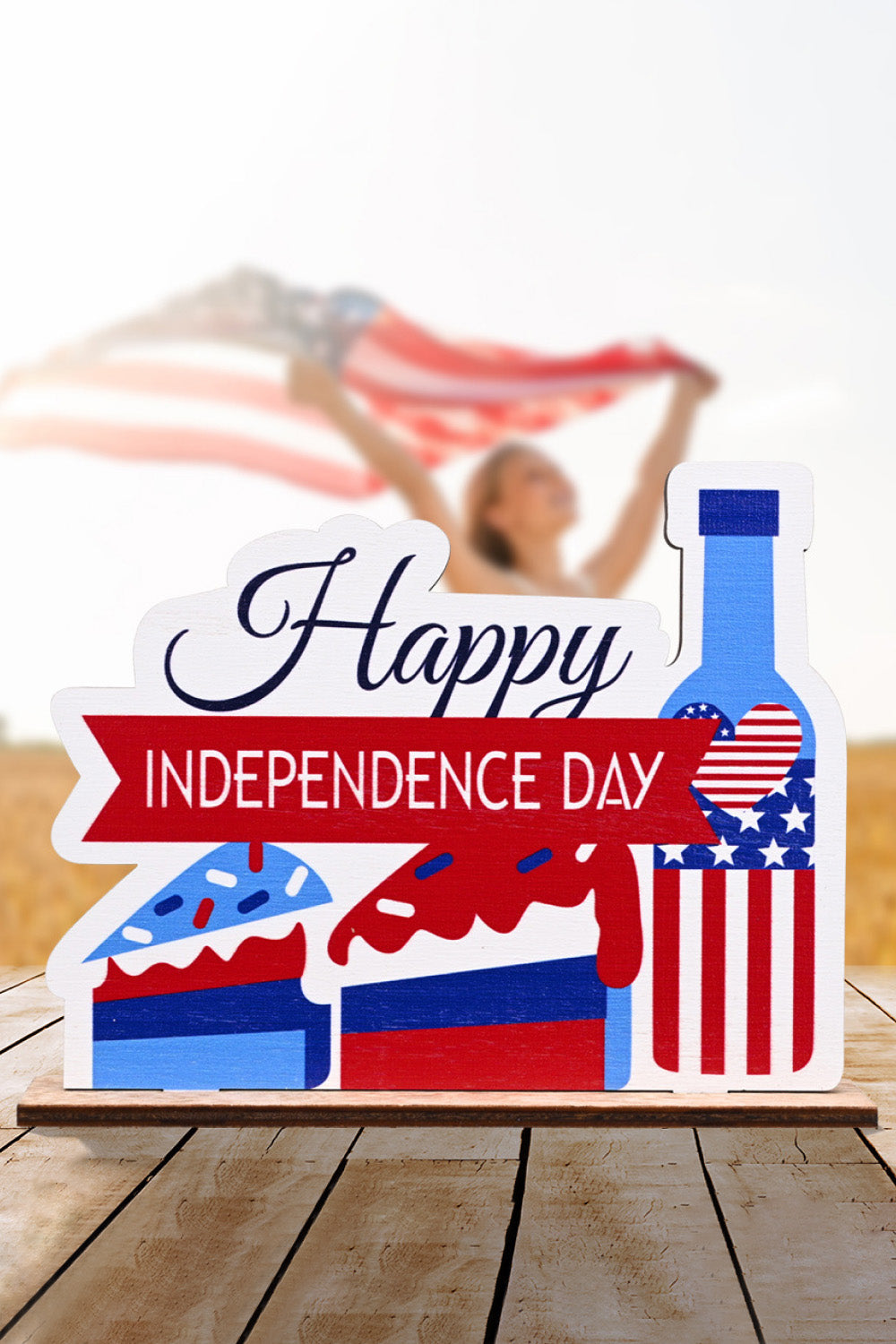 Patriotic wooden tabletop decor with "Happy Independence Day" text, cake slices, and a bottle with USA flag design.