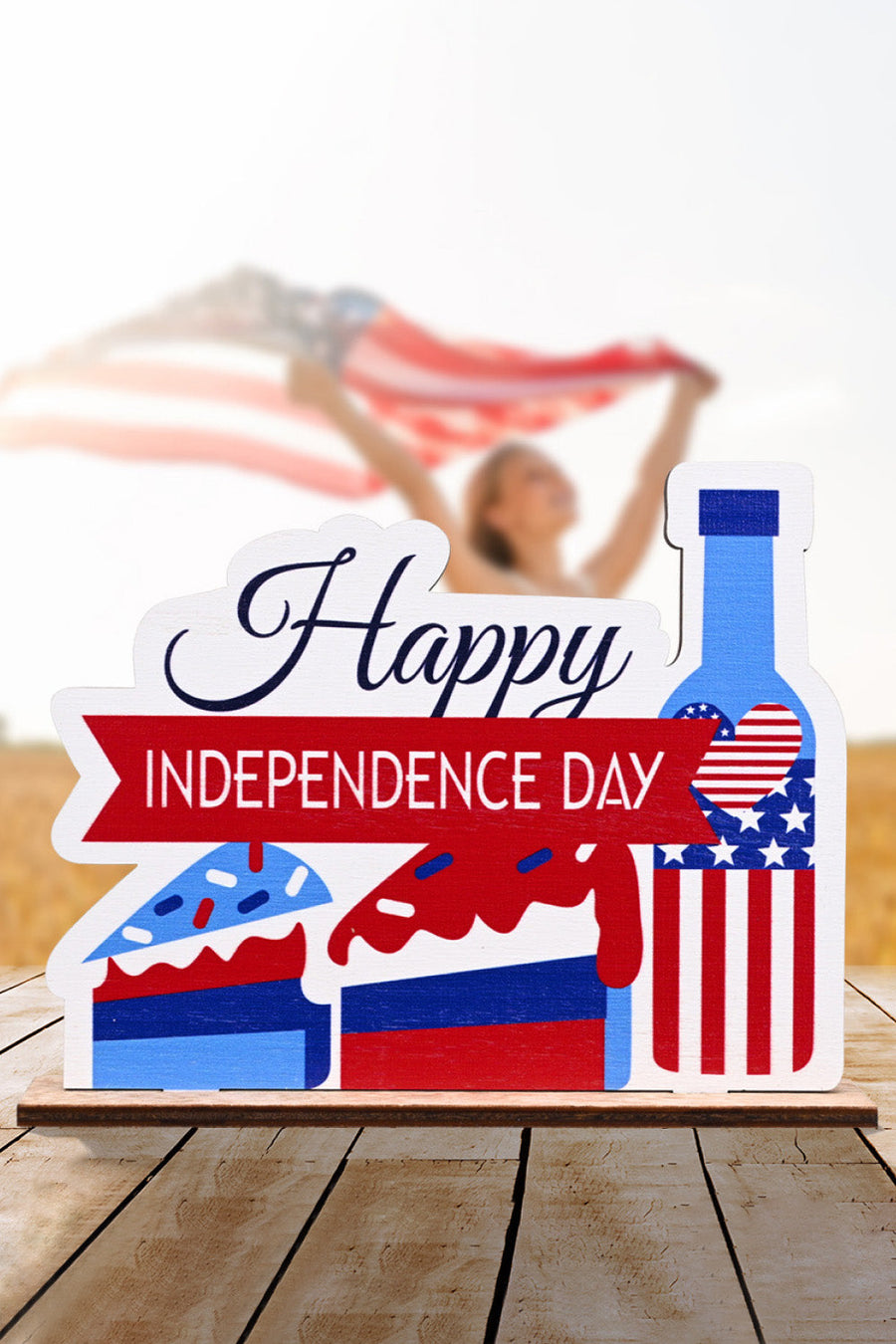 Patriotic wooden tabletop decor with "Happy Independence Day" text, cake slices, and a bottle with USA flag design.