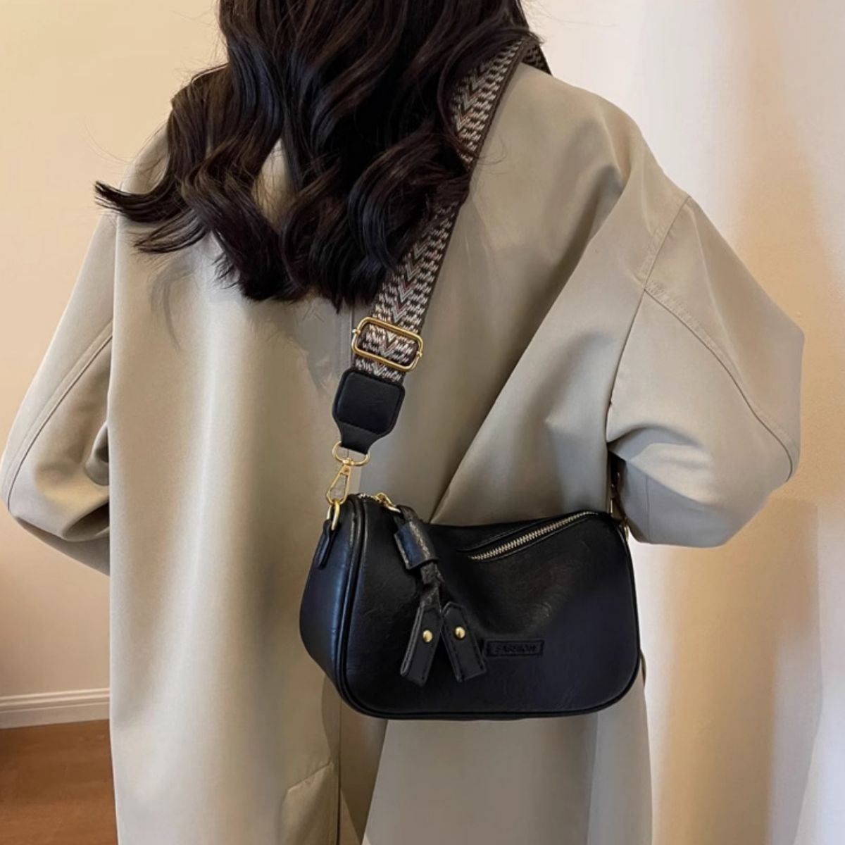 Black textured PU leather crossbody bag with tassel detail and patterned strap.