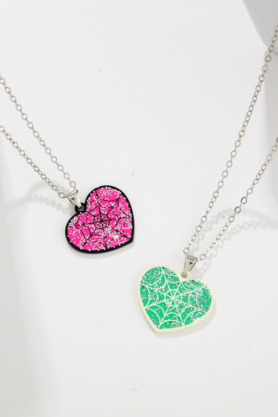 Spooky season heart necklaces with spiderweb design and glitter detail in pink and green.