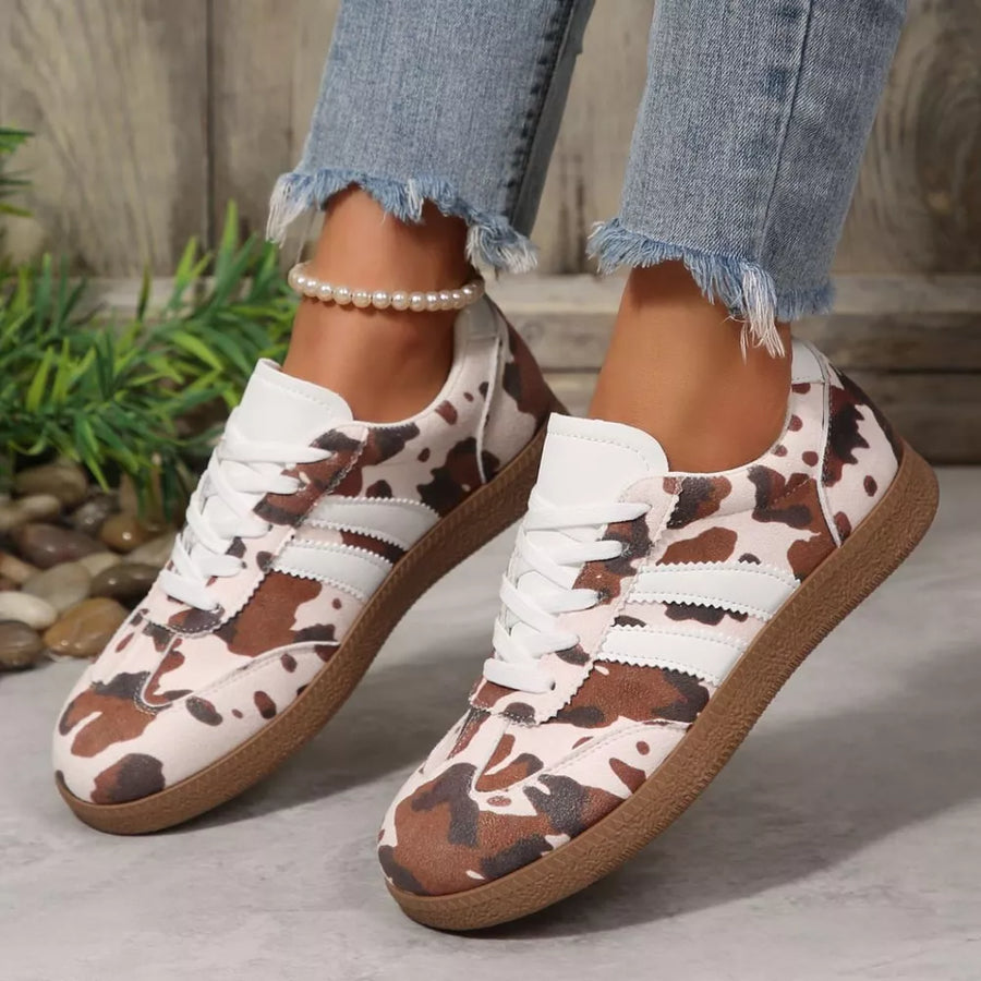 Trendy cow print low-top sneakers with white laces and brown soles.