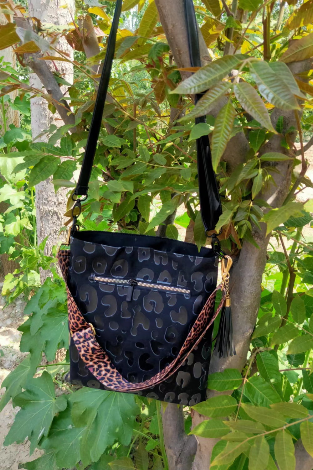 Black crossbody bag with embossed leopard print and tassel detail.