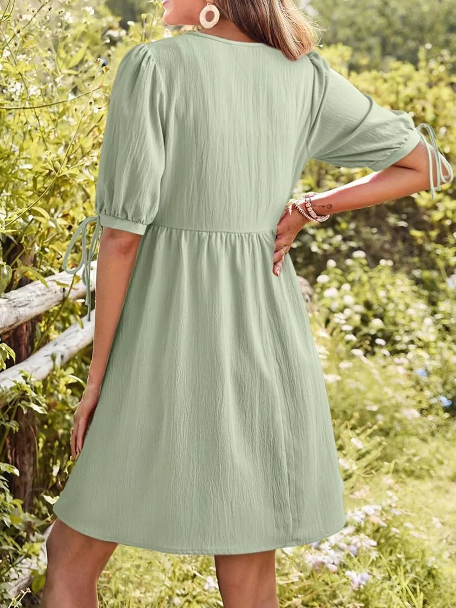 Light green tied neck puff sleeve mini dress with textured fabric and tie details on sleeves.