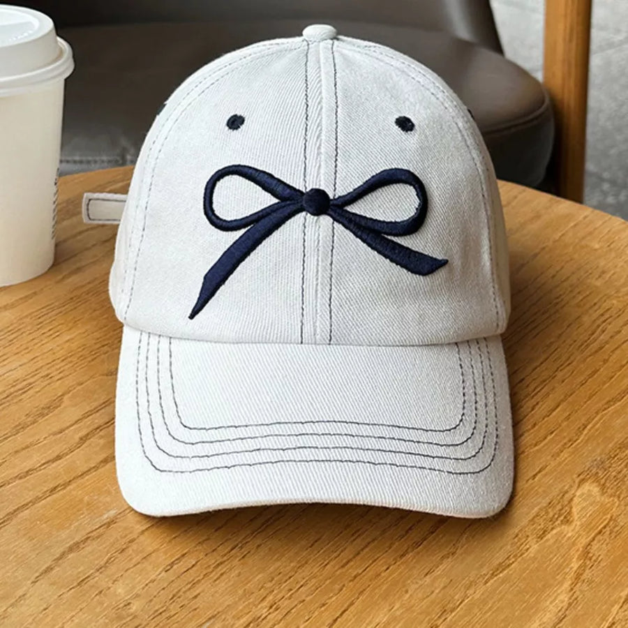 White baseball cap with embroidered dark blue bow accent and stitching details.