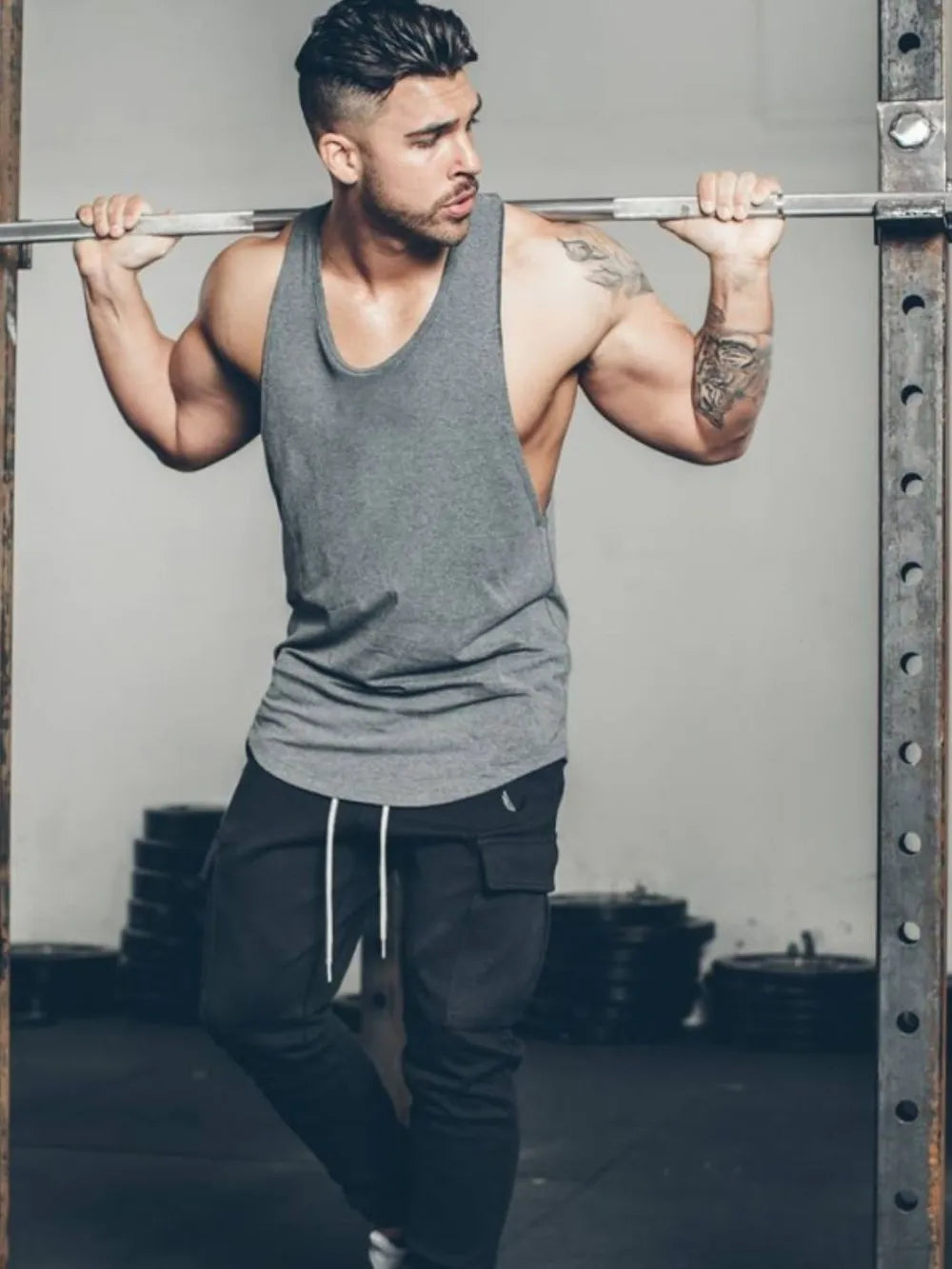 Scoop neck muscle tank top in dark gray with a relaxed fit, worn by a man in a gym.