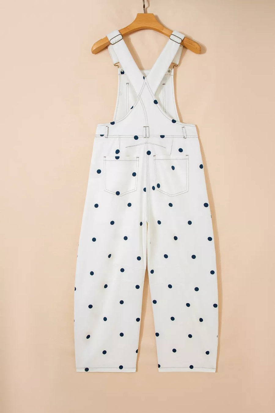 White denim overalls with navy polka dots, featuring buttoned straps and back pockets.