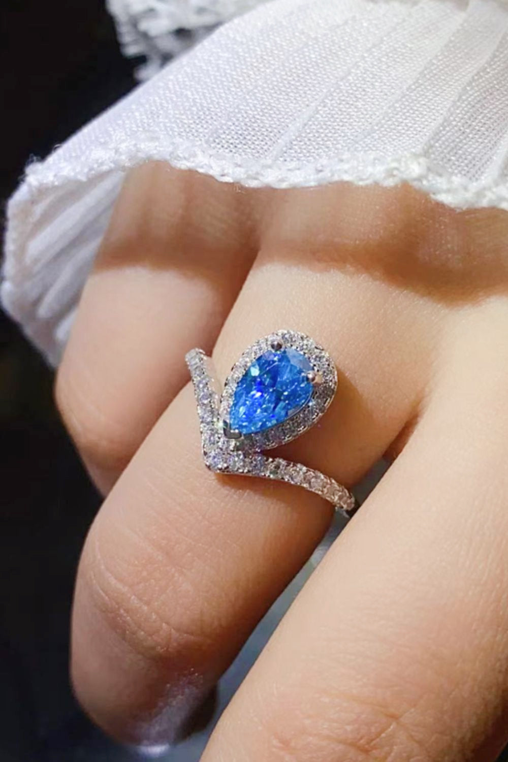 Sky blue pear halo ring with chevron band, detailed with small clear stones.