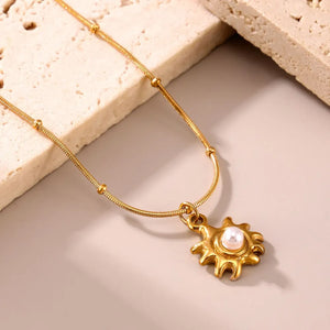 Gold sunburst pendant necklace with pearl detail and beaded chain.