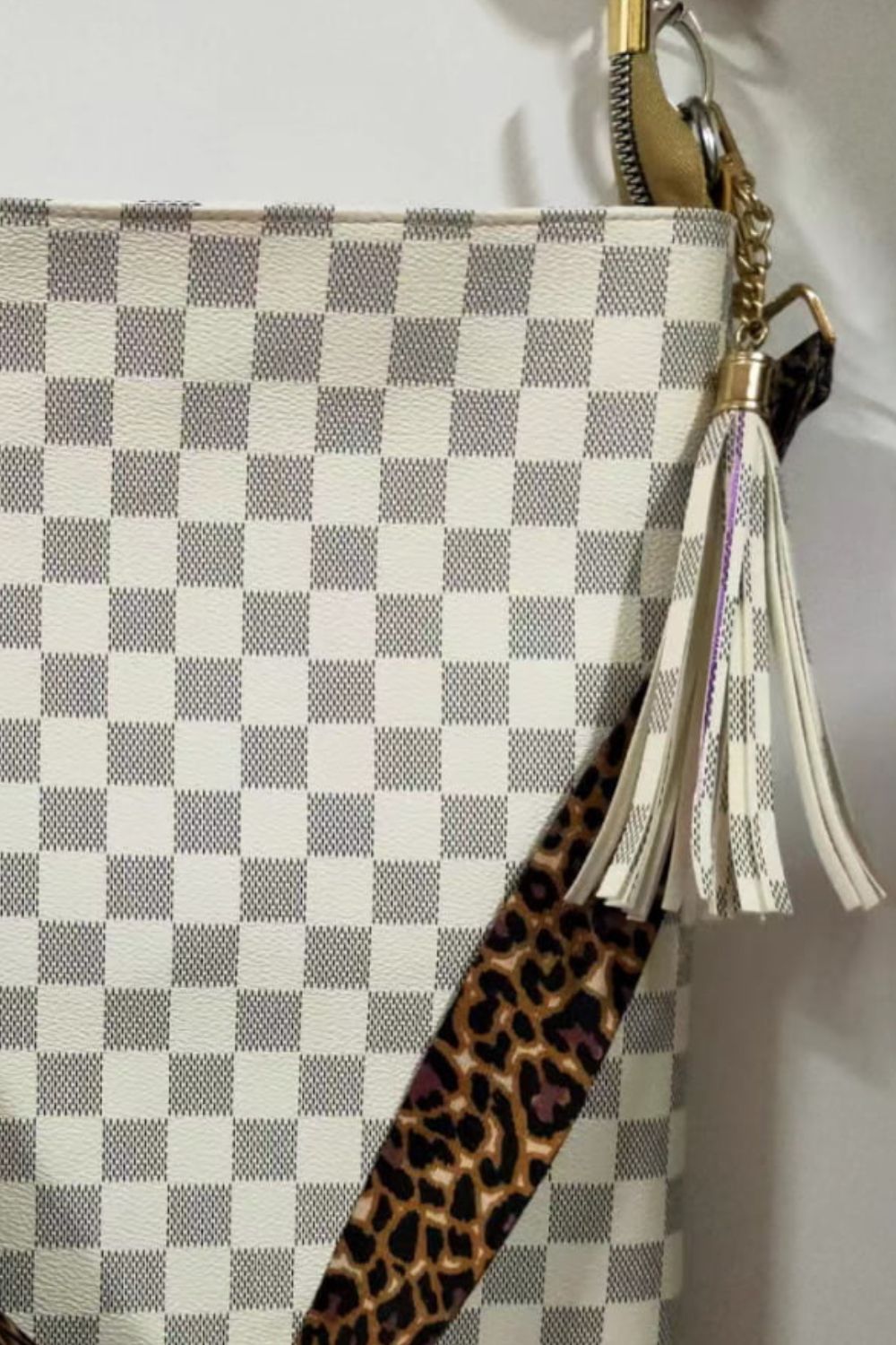 Cream checkered crossbody bag with leopard print strap and tassel detail.