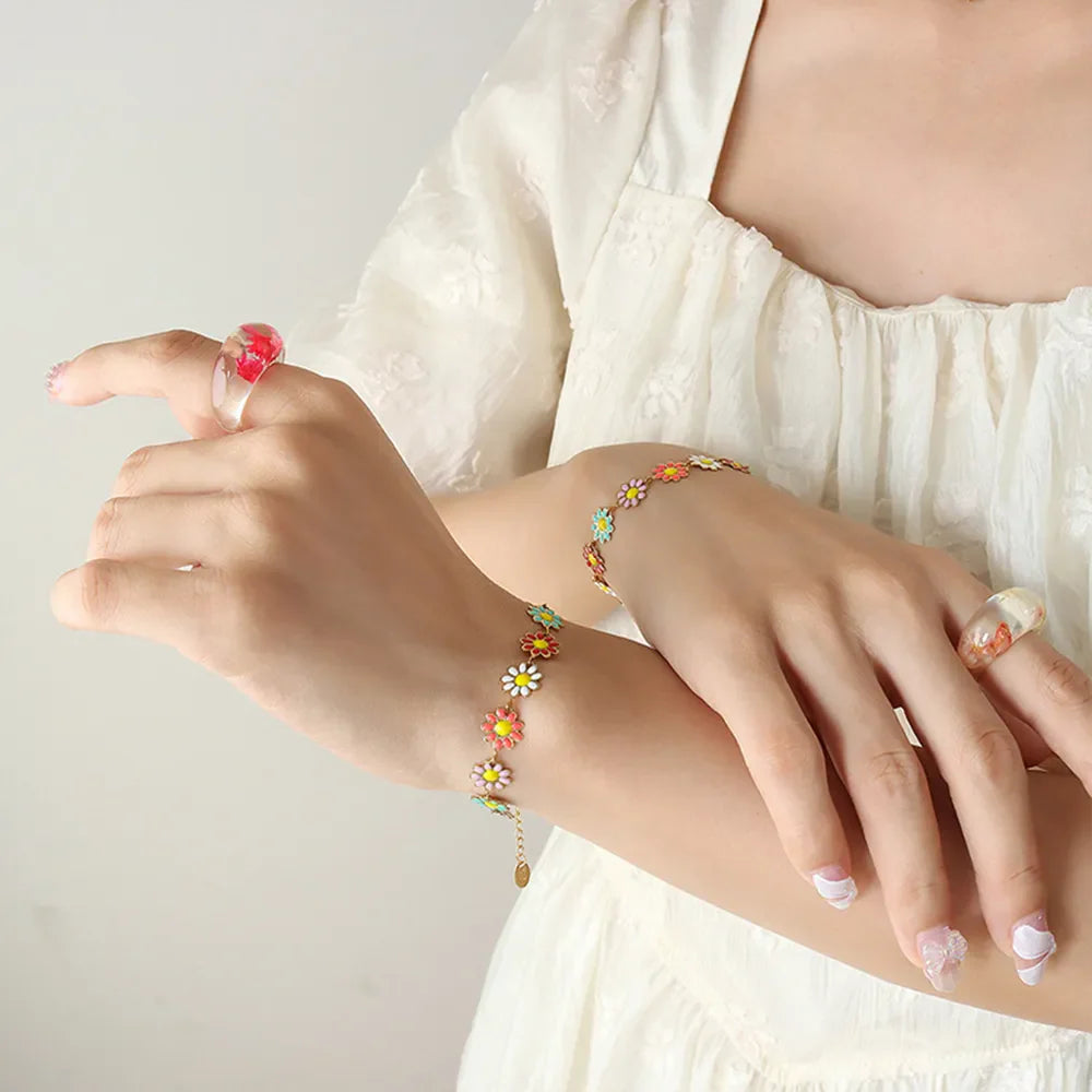 Gold metal bangle bracelet with colorful daisy charms and a delicate chain bracelet with matching flower charms.