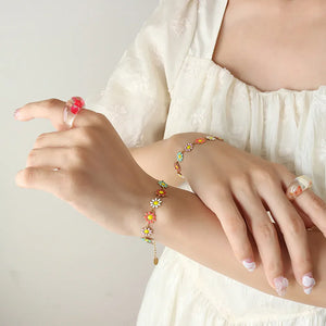 Gold metal bangle bracelet with colorful daisy charms and a delicate chain bracelet with matching flower charms.