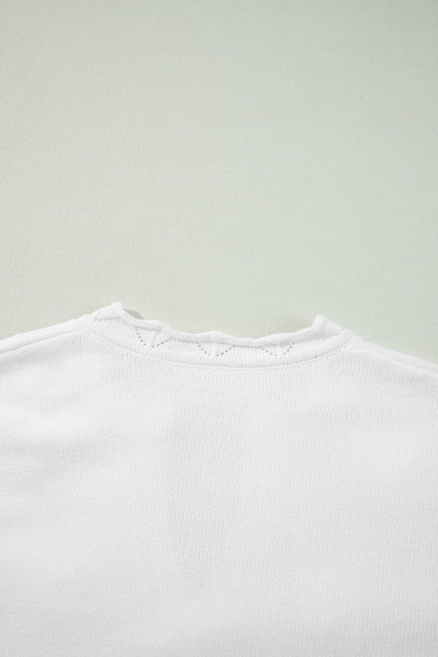White knit sweater with scalloped notch neck detail and subtle eyelet pattern.