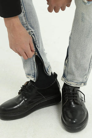 Light wash distressed skinny jeans with ankle zippers shown being zipped up.